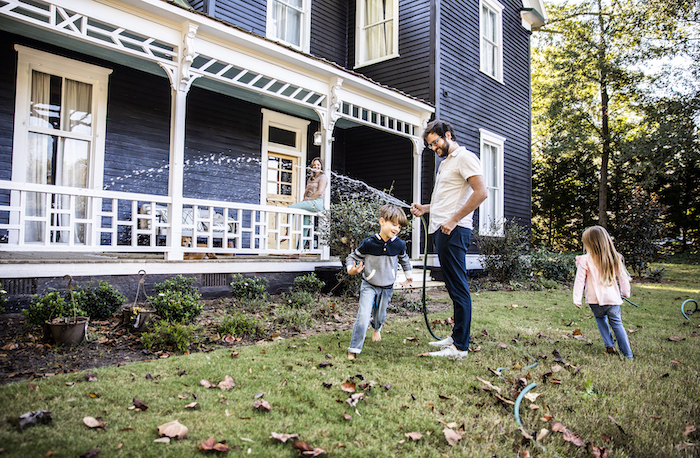 family watering yard in front of older home
